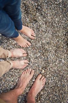 The feet of all the family members on the pebbly shore of the sea.