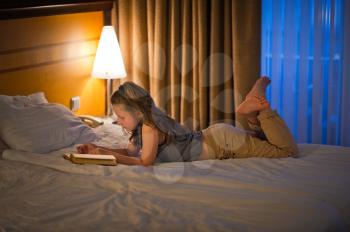 The child enjoys reading a book while lying in bed.