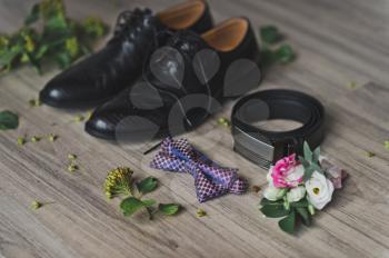 Strap, tie, shoes and a boutonniere on the table.