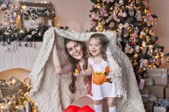 Daughter with mother play around the Christmas tree.