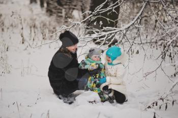 Mother with two children walking on the background of snowy forest.