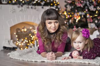 The child with the mother sitting on a white Mat around the Christmas tree.