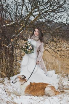 Portrait of a bride on a walk with a dog on a winter field background.