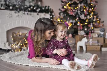 Portrait of mother with her daughter play near the fireplace and Christmas tree.