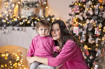 Portrait of mother with daughter on the Christmas tree in sparkling lights.