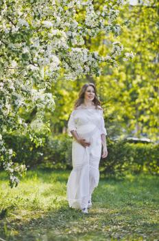 Pregnant girl walks thoughtfully on a spring blossoming garden.