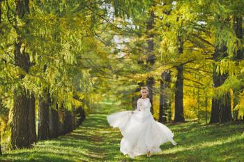 Bride spinning in the developing white dress on background of the forest alleys.