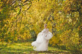 The bride happily spinning in the developing dress on the edge of the bright autumn forest.
