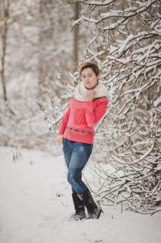 The photo of the girl in the pink sweater on the background of snowy trees.