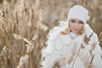 Girl in a white furry coat stands in the middle reeds in the winter.