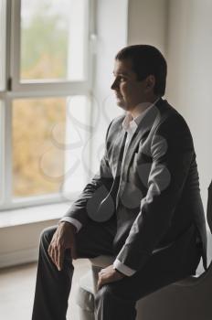 The groom in a business suit sitting at a huge lit window.