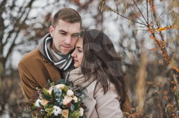 Portrait of a young couple in winter outfits among the branches of sea buckthorn.