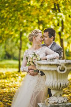 The gentle embrace of the newlyweds on the background of beautiful autumn garden.