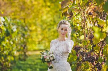 Portrait of a bright young bride amid manicured rows of the vineyard.