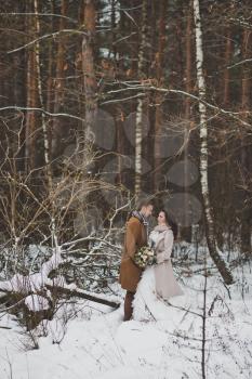 Newlyweds admire each other standing in the winter forest.