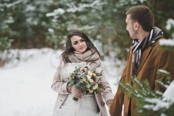 Newlyweds walk among snow-covered trees and pines.