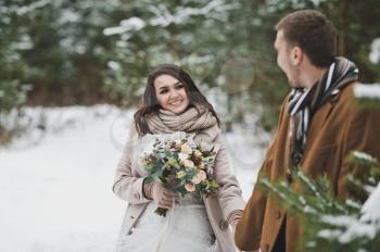 Newlyweds walk among snow-covered trees and pines.