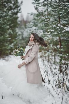 Portrait of a bride in a chic white dress among snow-covered fir branches.