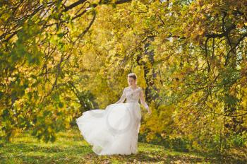 Portrait of a bride in a white dress swirling in the meadow autumn forest.