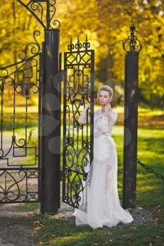 Portrait of a bride in a rich white dress facing the iron gate.
