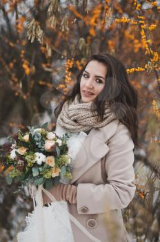 Close-up portrait of bride with a bouquet of winter among the branches of sea buckthorn.