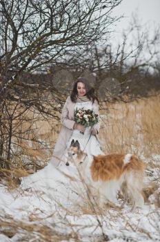 Portrait of a bride on a walk with a dog on a winter field background.