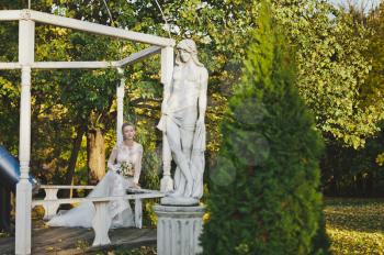 Portrait of bride in wedding dress near the statue in the garden.