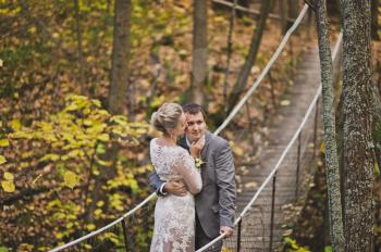 The bride and groom in beautiful outfits are on long wobbly suspension bridge.
