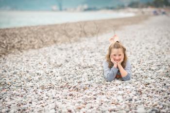 The child is lying on the pebbles of the marine beach.