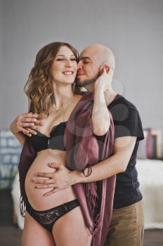 A man gently hugs and strokes his pregnant woman.
