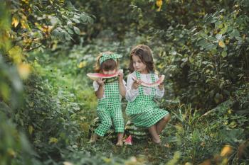 Two sisters outdoors eating watermelon.
