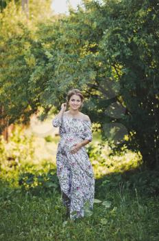 Portrait of a pregnant girl walking in the summer garden.