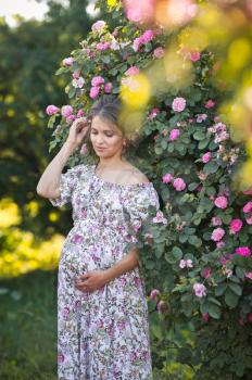 The girl in the position of pregnancy in nature in a free colorful dress.