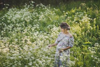 Portrait of a happy pregnant woman in a clearing of white flowers kupyr forest.