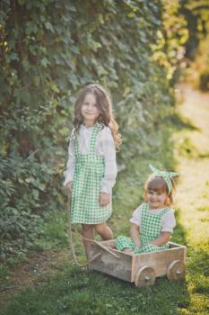 Two sisters play outside with a cart.