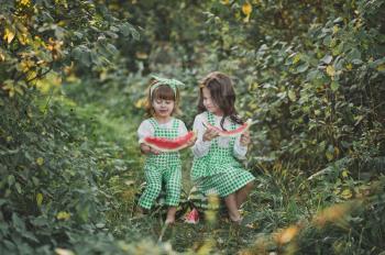 Sisters sit on watermelons among alleys and eat watermelons.