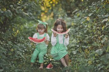 Sisters sit on watermelons among alleys and eat watermelons.