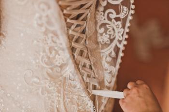 A friend helps the bride to wear a wedding dress.