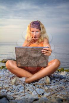 Girl with surprise looks in the laptop at the beach