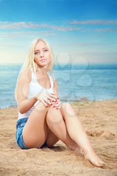 beautiful young blond woman in shorts and t-shirt sitting sunning sea. summer rest