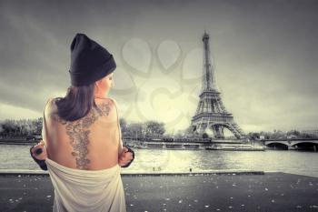 girl with a tattoo stands on the banks of the Seine near the Eiffel Tower. dramatic portrait
