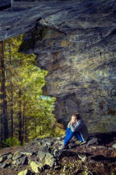 girl in a cave sits and looks at access to the forest