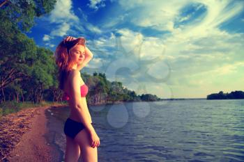 beautiful sexy woman in a swimsuit on the sea coast in summer evening. the trees on the ocean