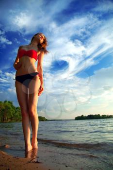 beautiful sexy woman in a swimsuit on the sea coast in summer evening. the trees on the ocean