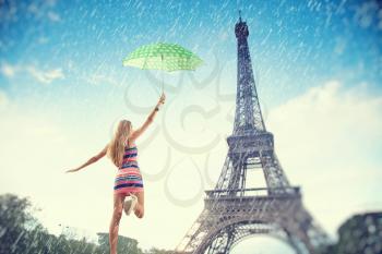 Beautiful girl running with an umbrella in the rain on a background of the Eiffel Tower. Summer trip to France in Paris.