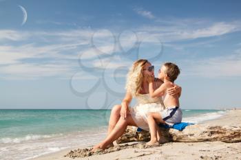 son kissing mom, they sit on the beach, past the boat floats