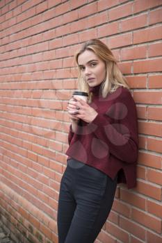 girl with a glass of coffee near a brick wall