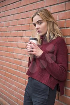 girl with a glass of coffee near a brick wall
