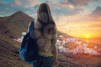 girl with a backpack looking at the city on the coast at sunset