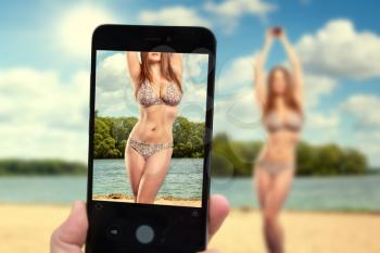 blogger takes pictures on a smartphone girl in a bikini on the beach